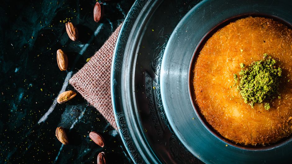 Kunefe doré dans un plat en cuivre, garni de pistache concassée