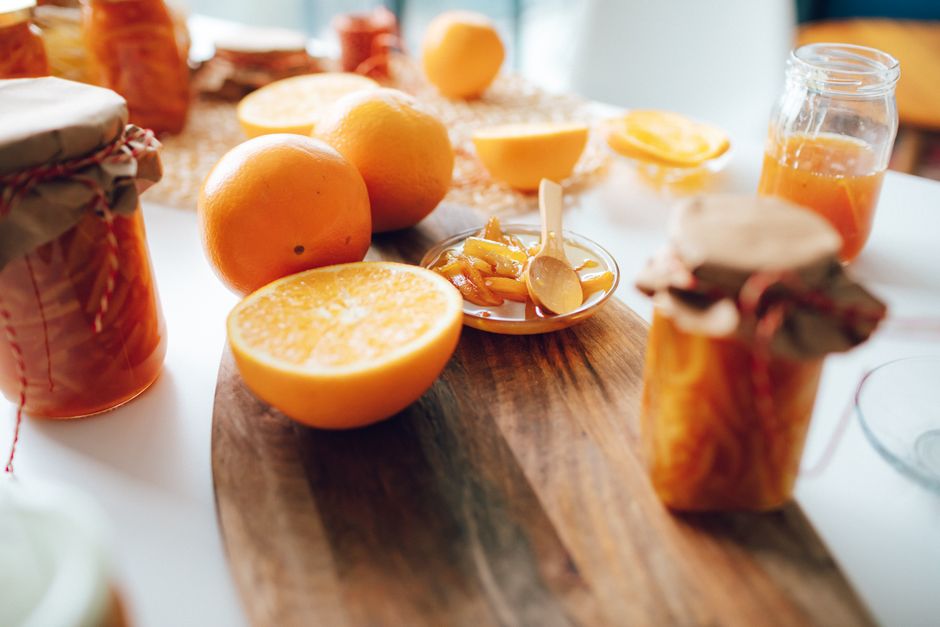 Pots de confiture maison à l'orange entourés d'agrumes frais sur une planche en bois