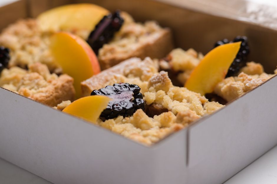 Parts de crumble aux fruits présentées dans une boîte à pâtisserie